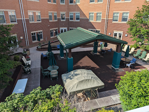 A serene courtyard featuring a green pavilion and comfortable seating surrounded by brick buildings.