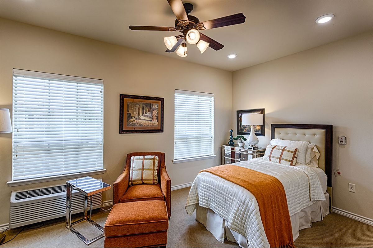 A cozy bedroom with warm decor, featuring a bed, chair, and ceiling fan.