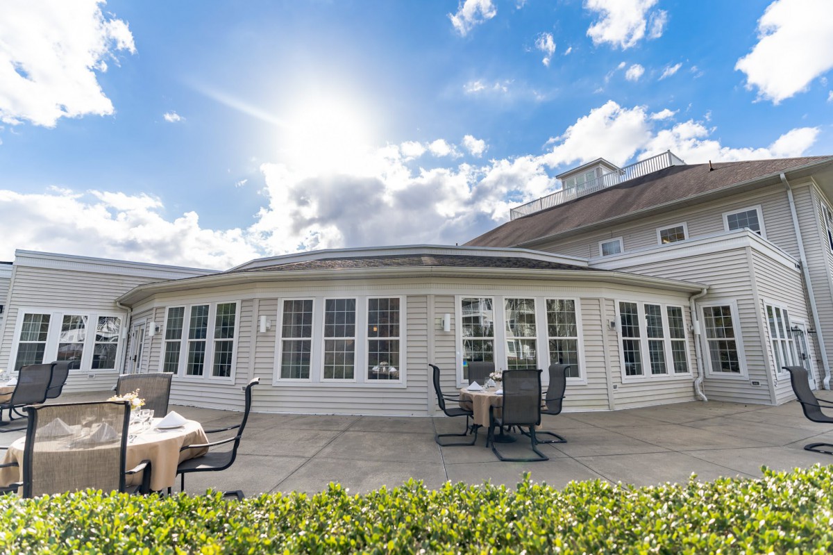 A sunlit patio area with tables and chairs outside a white building.