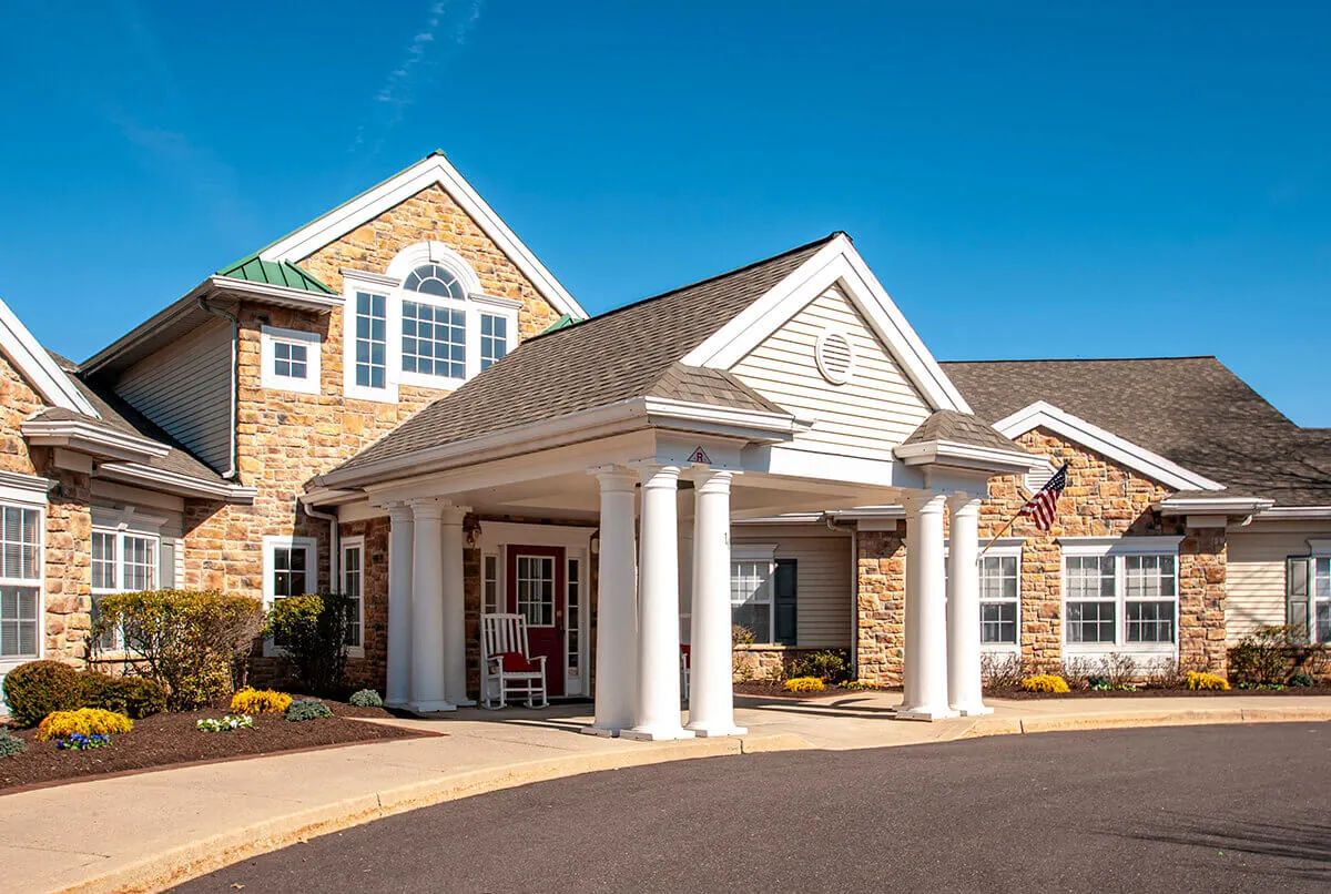 A well-maintained building with a central entrance featuring columns and a stone exterior, set against a clear blue sky.