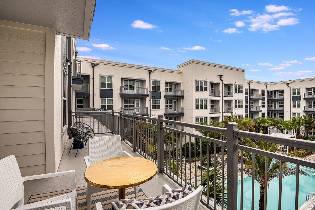 A modern balcony overlooking a swimming pool and adjacent apartment complex.
