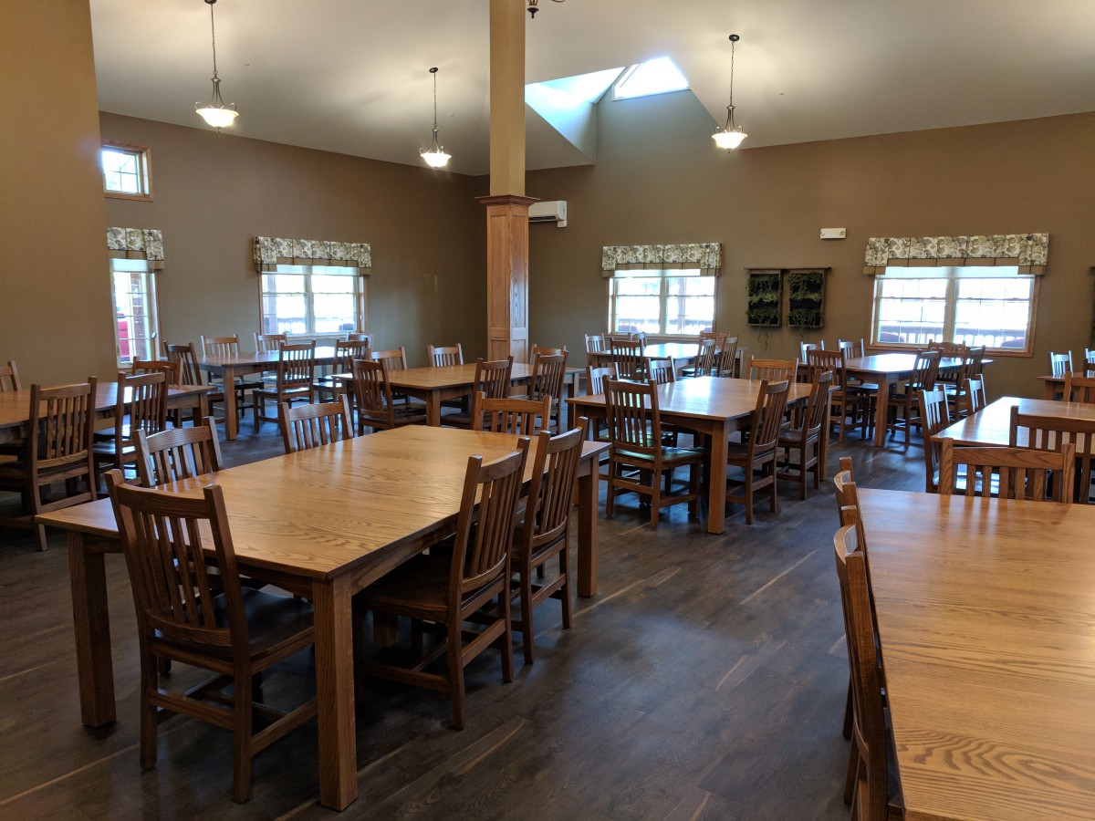 An empty dining hall with wooden tables and chairs arranged neatly.