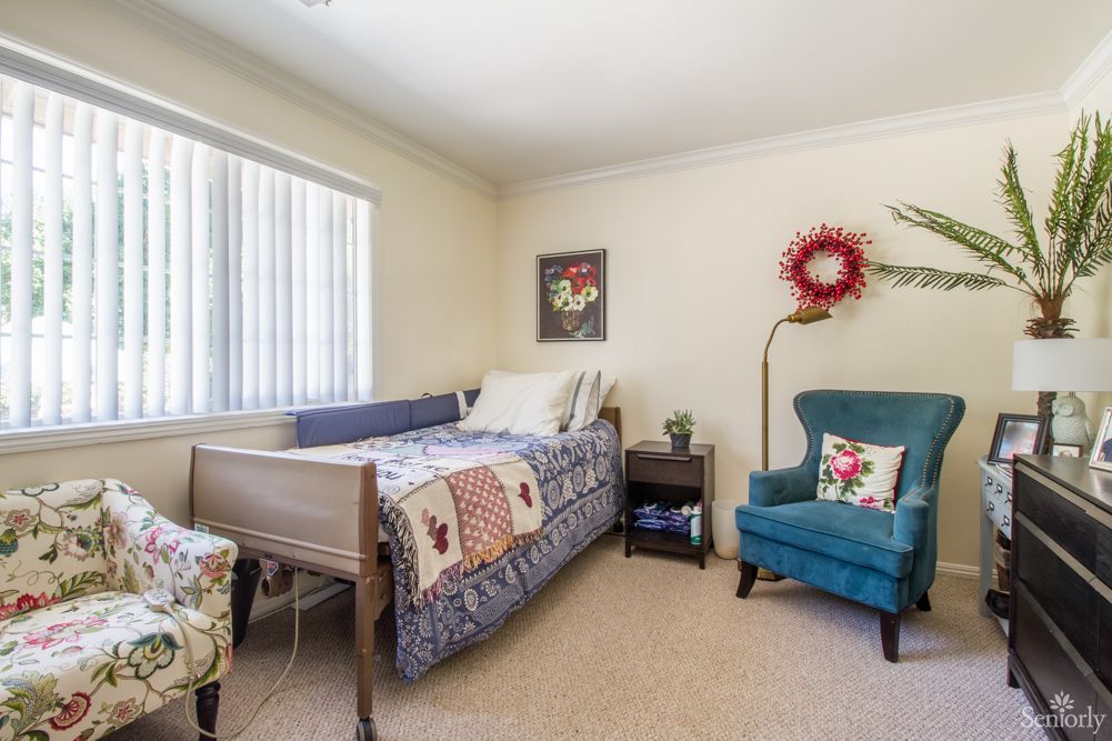 A cozy bedroom with a bed and a teal armchair, decorated with colorful quilts and wall art.