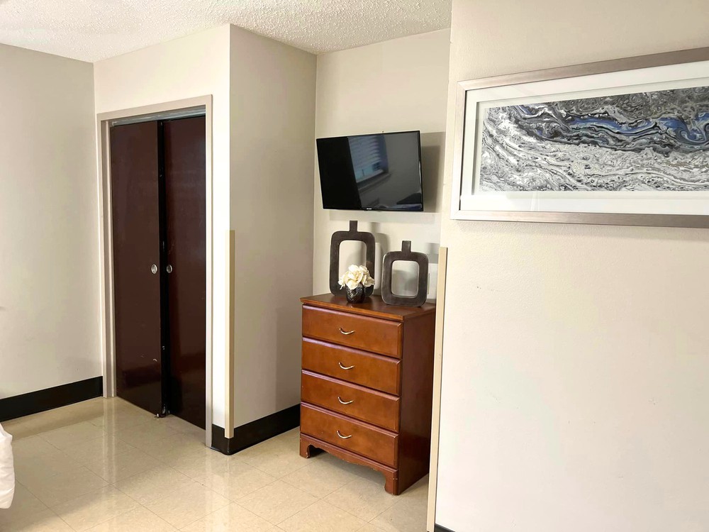 A modern bedroom corner featuring a wooden dresser, a wall-mounted TV, and framed artwork.