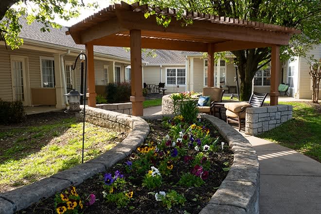 A beautiful garden with vibrant flowers and a shaded seating area under a pergola.