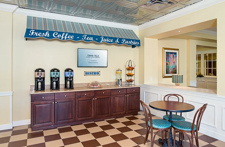 A cozy coffee and beverage station with a checkered floor, featuring self-service options for coffee, tea, juice, and pastries.