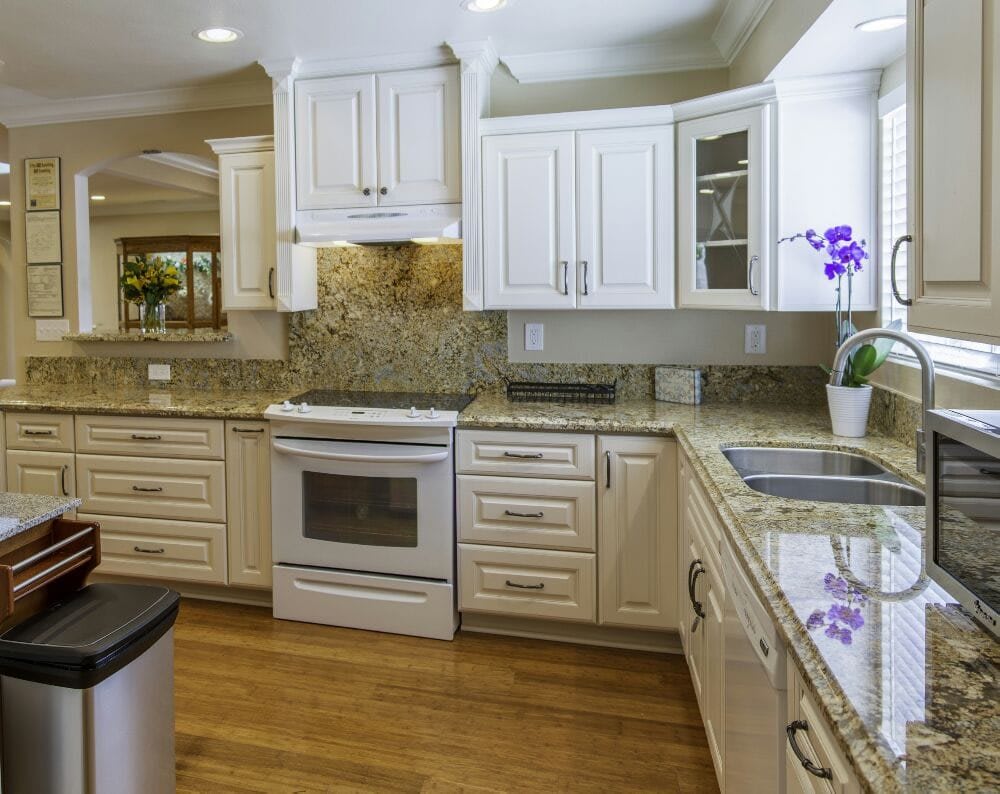 A modern kitchen with white cabinets, an oven, and hardwood flooring.