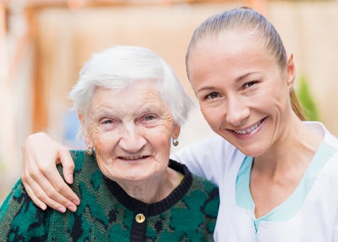An elderly woman and a younger woman smiling together, showcasing warmth and togetherness.