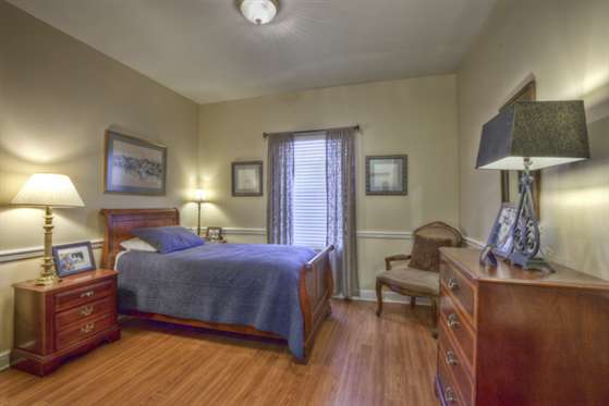 A cozy bedroom featuring a wooden bed and dresser, with soft lighting from a lamp next to the bed.