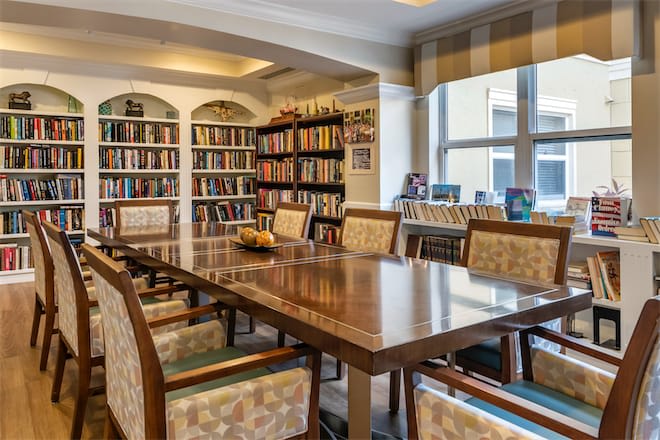 A cozy library meeting room with a large wooden table surrounded by chairs and shelves filled with books.