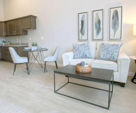 A modern, minimalist living room with a sofa and coffee table, featuring decorative artwork and an adjacent dining area.