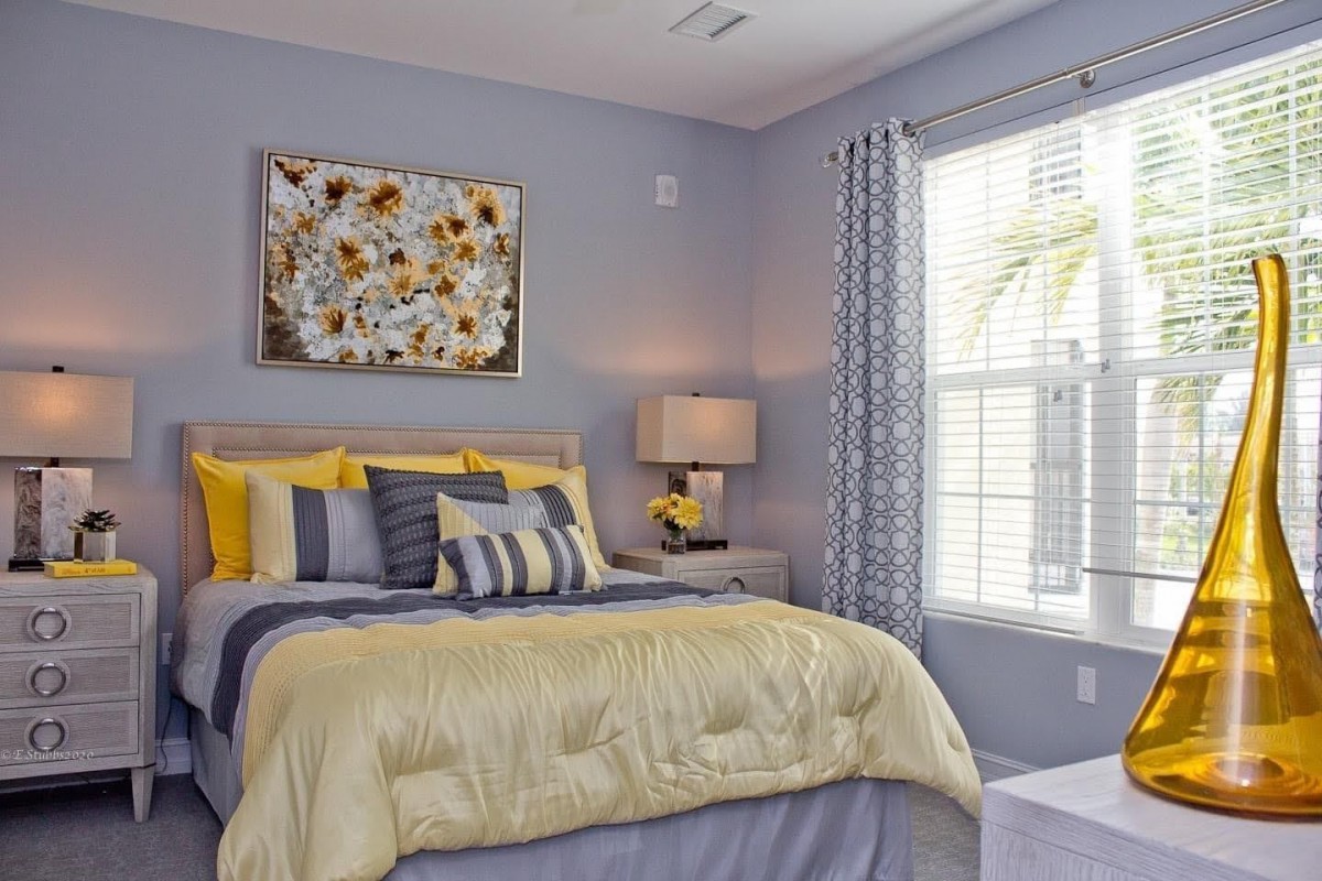 A cozy bedroom featuring a neatly made bed with yellow and gray bedding, complemented by a stylish lamp and artwork on the wall.