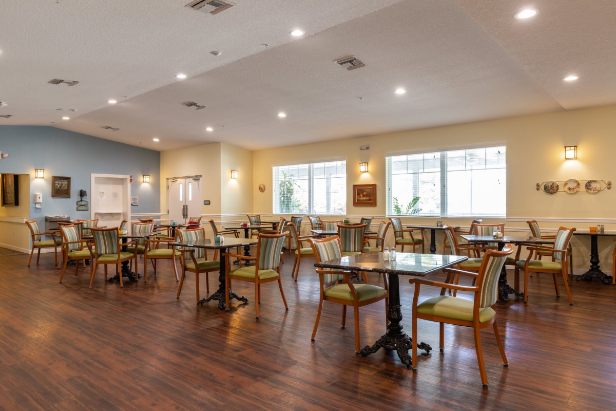 An elegant dining area with neatly arranged tables and chairs, featuring wooden flooring and ample natural light.