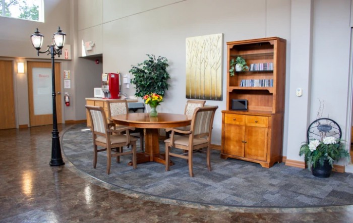 A cozy corner featuring a wooden dining set and shelves, complemented by a decorative plant and a vase of flowers.