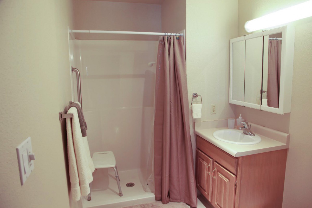 A bathroom featuring a shower with a curtain, a sink with a mirror above it, and towels hanging on the wall.