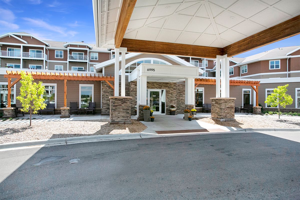 A modern building entrance featuring a covered driveway with stone pillars and large windows.