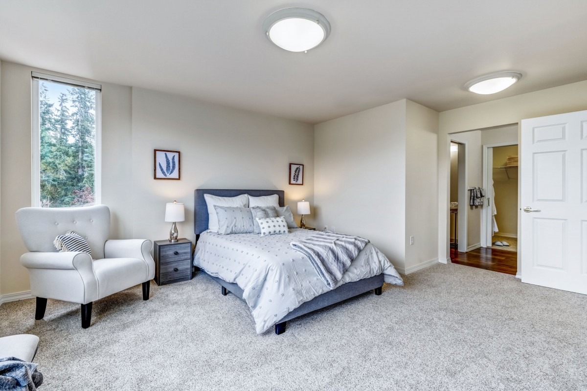 A modern bedroom with a neatly made bed, white armchair, and stylish decor.