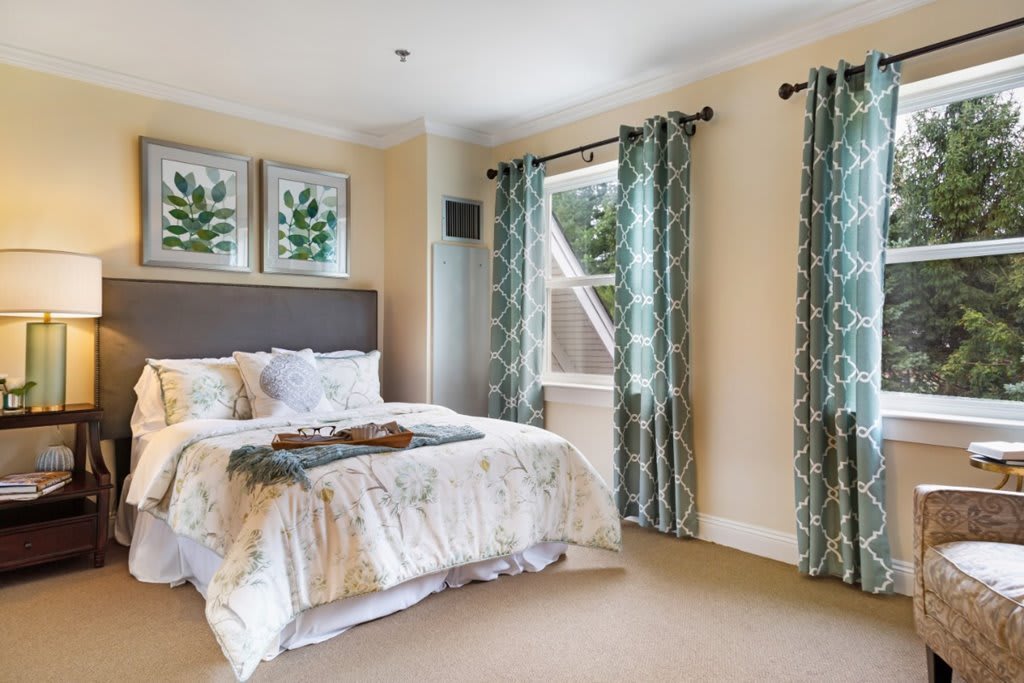 A cozy bedroom featuring elegant curtains, a comfortable bed, and framed artwork on the walls.