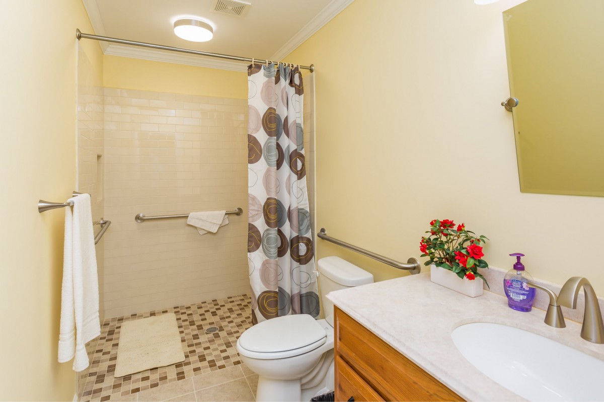 A well-lit bathroom with a shower, toilet, and sink, featuring a patterned shower curtain and decorative flowers on the countertop.