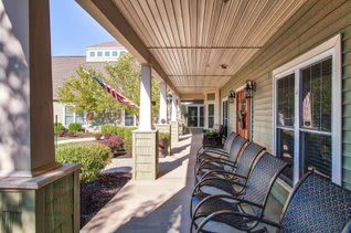 A sunlit porch with a row of chairs overlooking a garden and well-maintained landscaping.