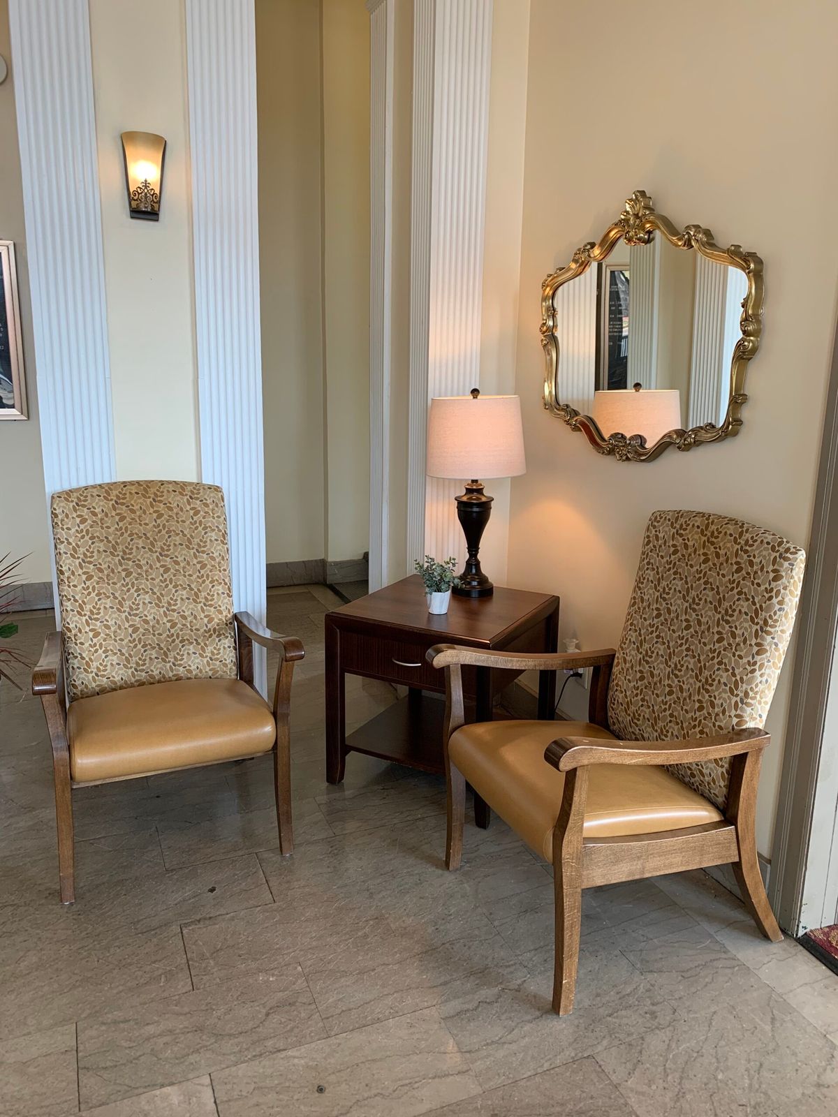 A cozy seating area with two armchairs, a small table with a lamp, and an ornate mirror on the wall.