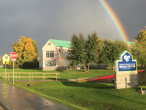 A picturesque scene featuring a building under a vibrant rainbow, surrounded by lush greenery and trees.