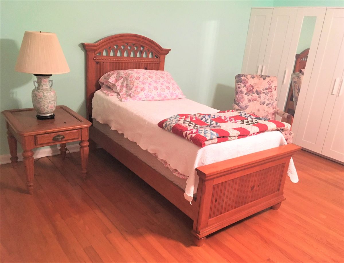 A cozy bedroom with a single wooden bed and matching nightstand.