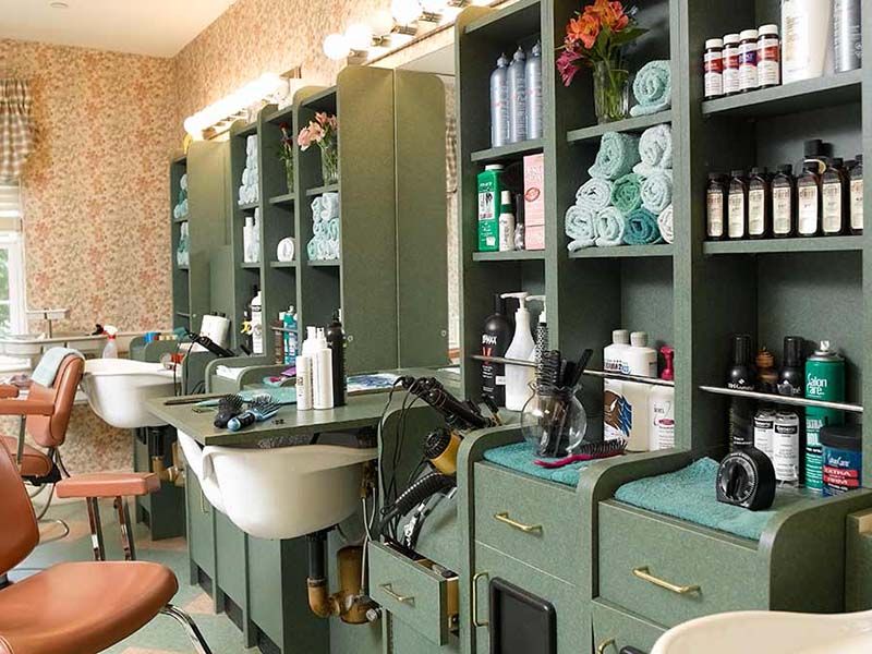 A stylish hair salon interior with green cabinetry and various beauty products neatly organized.
