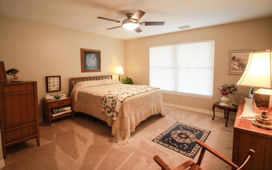 A cozy bedroom with a neatly made bed, carpeted floor, and warm lighting.
