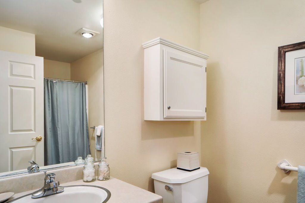 A clean bathroom with a sink, mirror, toilet, and wall-mounted cabinet.