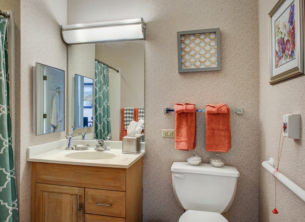 A neatly organized bathroom with a wooden cabinet, mirror, and orange towels hanging near the toilet.