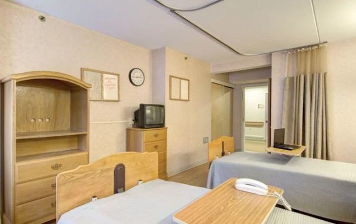 A hospital room with two patient beds and a television.
