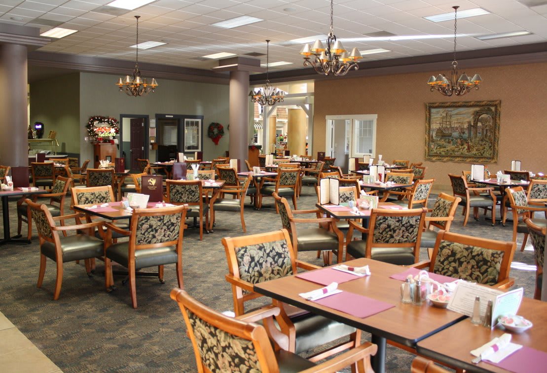 An elegantly decorated dining room with multiple tables and chairs, featuring chandeliers and a cozy atmosphere.