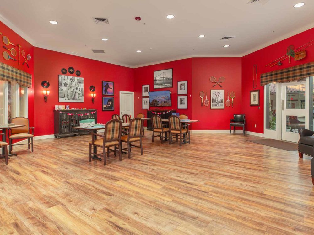 A spacious dining room with vibrant red walls, adorned with various artworks and wooden flooring.