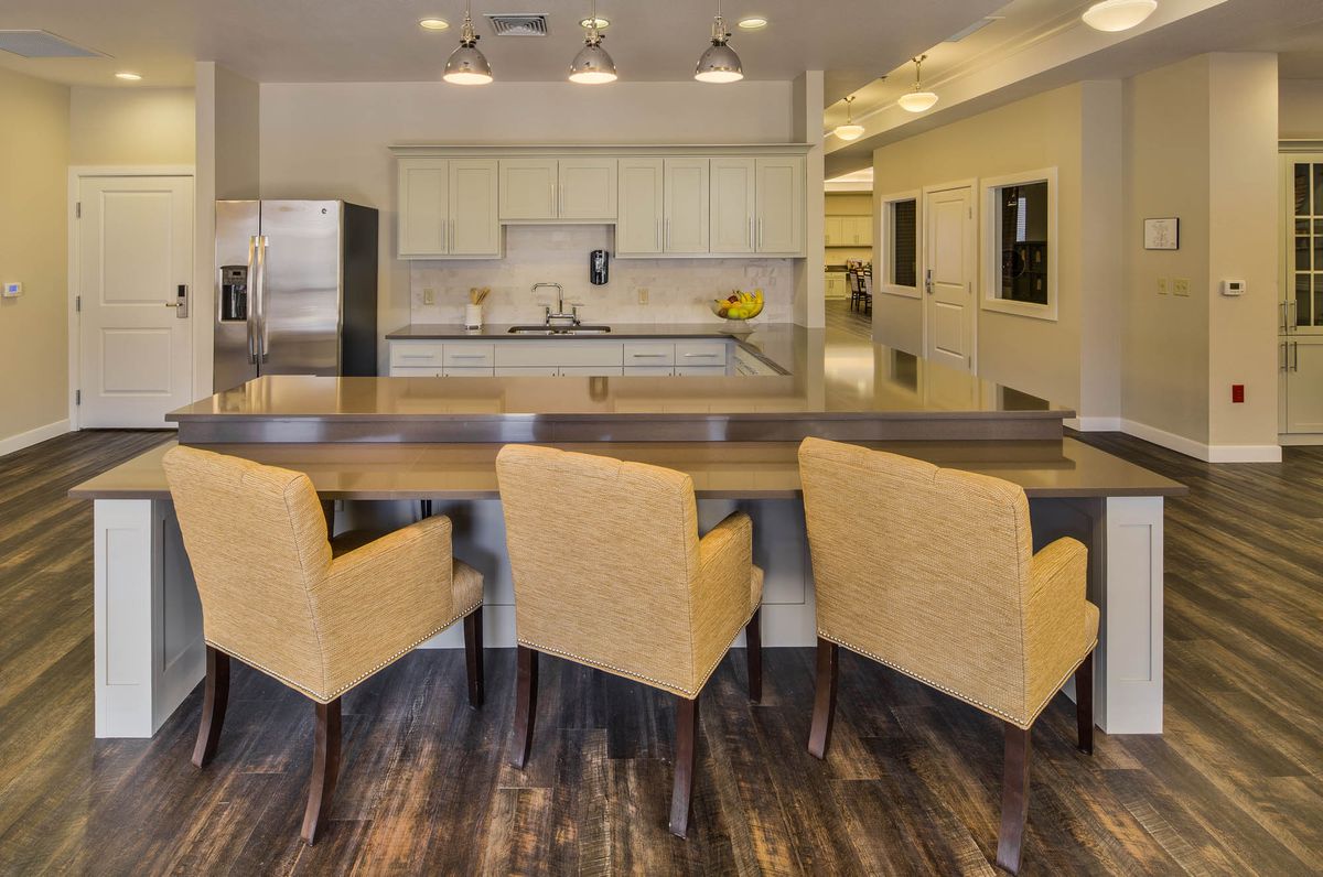 A modern kitchen with a large countertop and bar stools, featuring sleek appliances and open space design.