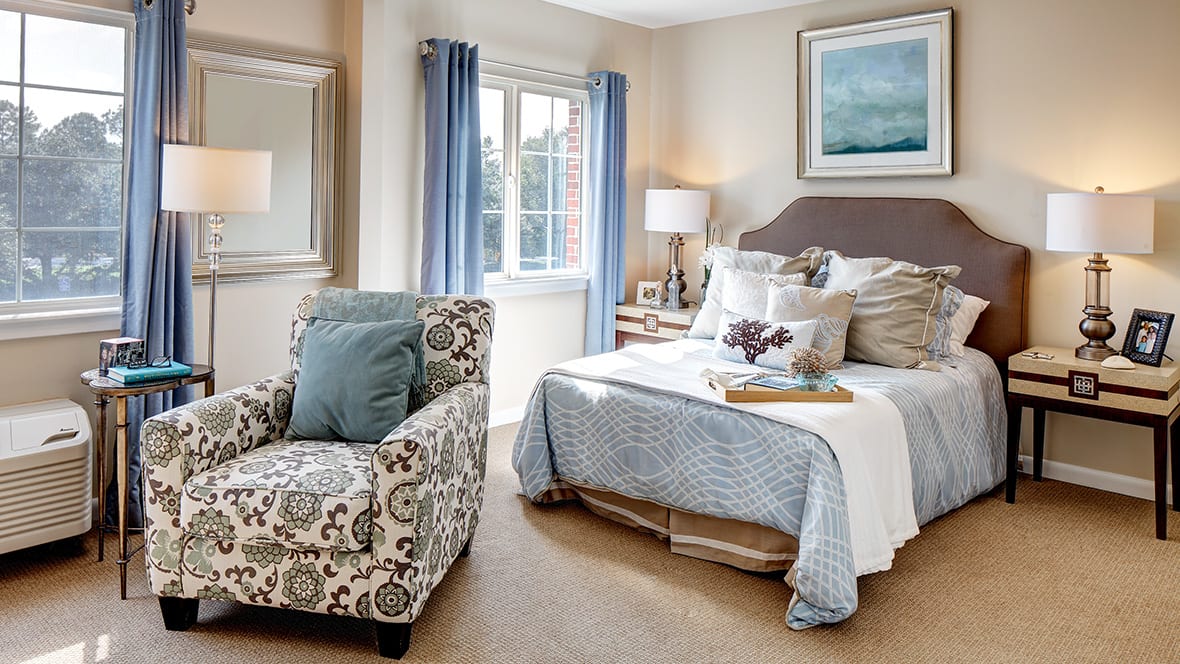 A cozy and stylish bedroom with a patterned armchair, comfortable bed, and soft lighting.