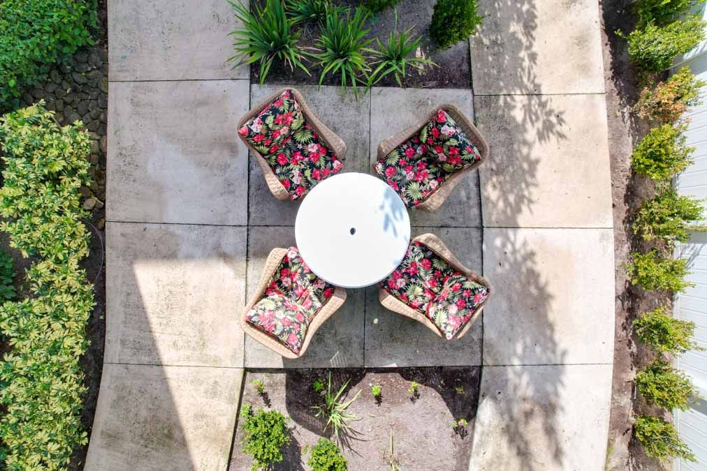Aerial view of a patio with a round table and four chairs featuring floral cushions, surrounded by plants.