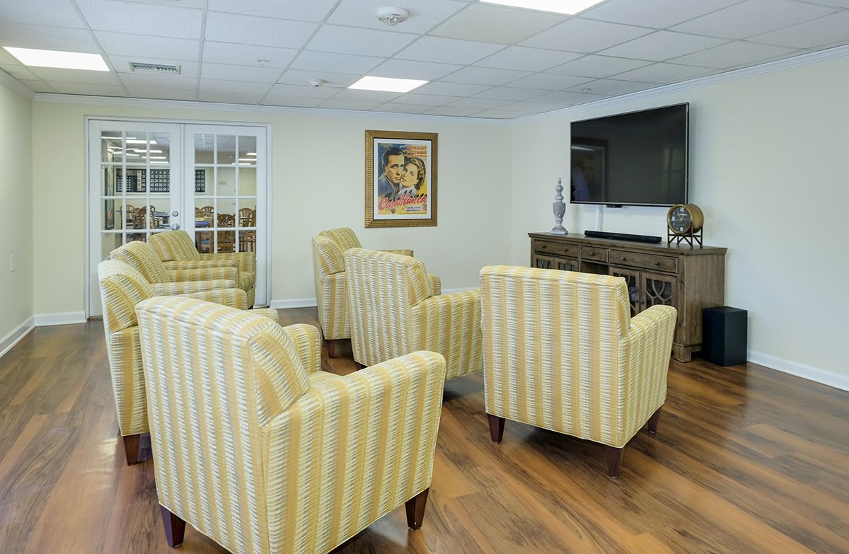 A cozy living room with striped armchairs facing a television, adorned with artwork and wooden flooring.