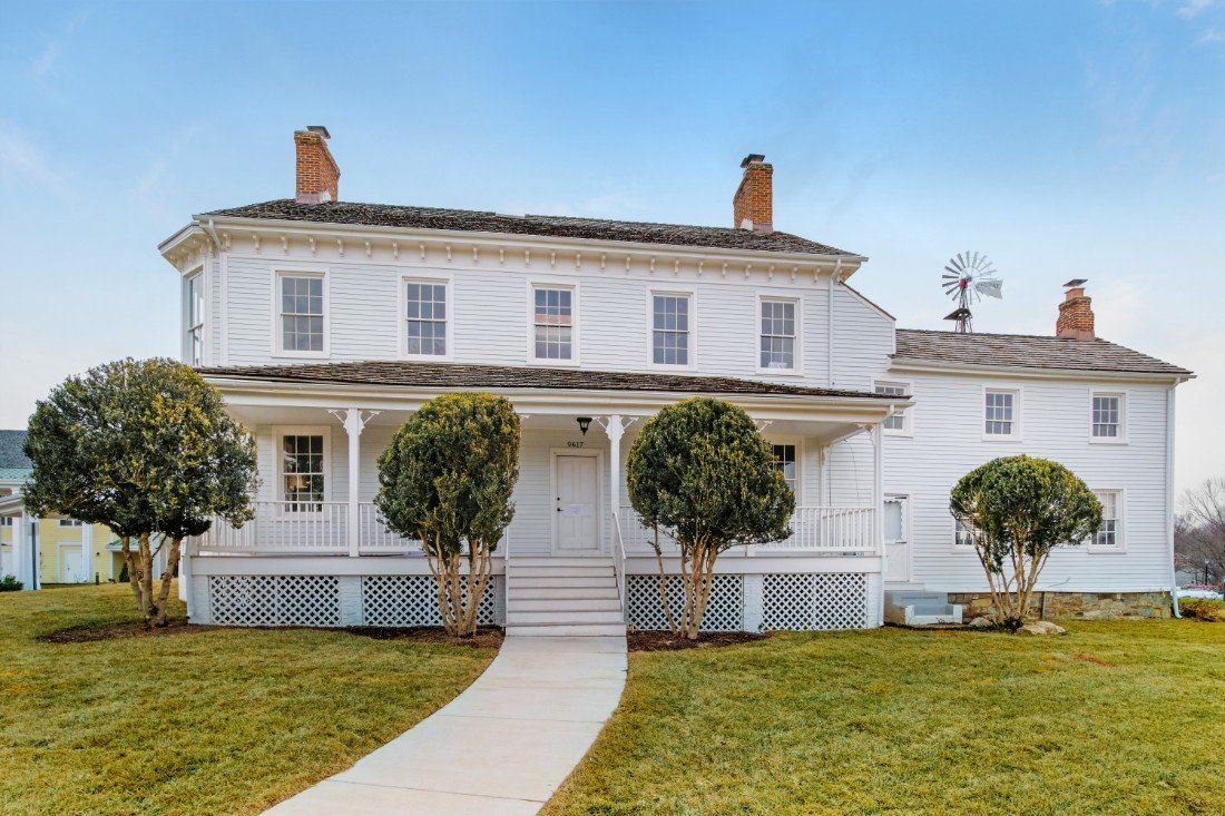 A large white house with a porch and trees in front, set on a well-maintained lawn.