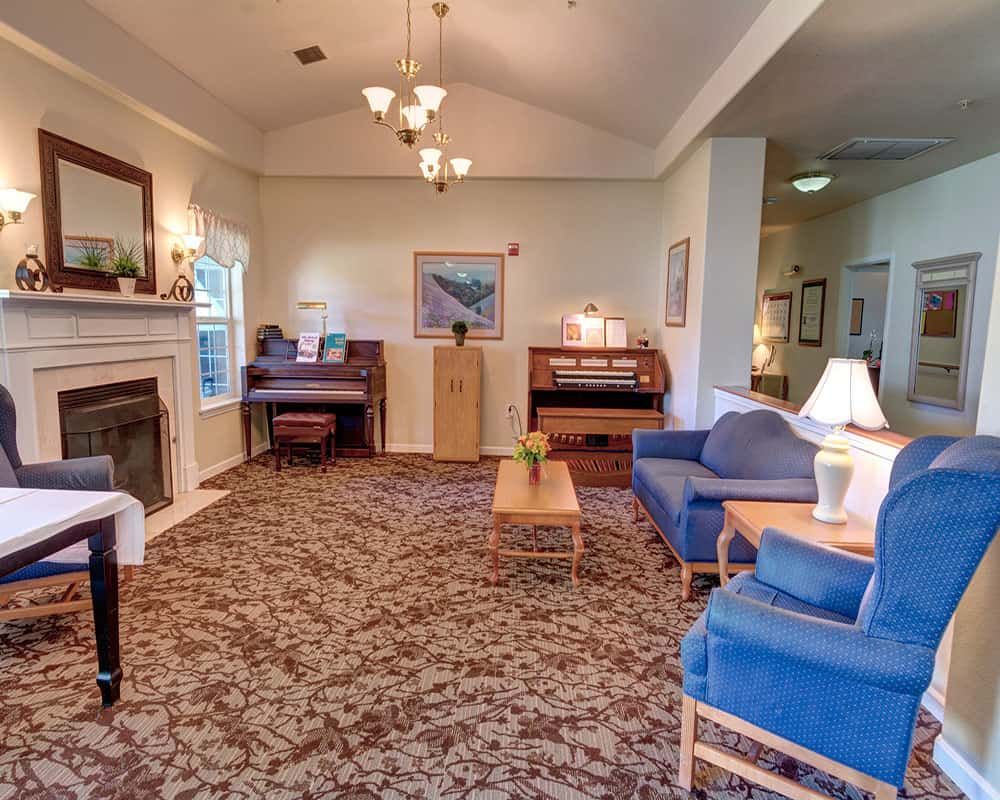 A cozy living room featuring a fireplace, blue sofas, a patterned carpet, and a piano.