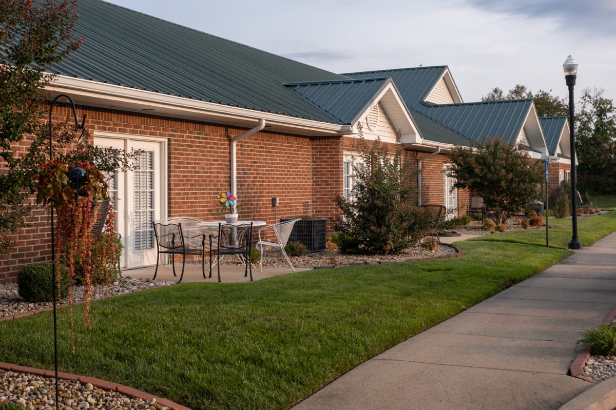 A row of brick houses with green roofs, featuring a well-kept lawn and patio furniture.