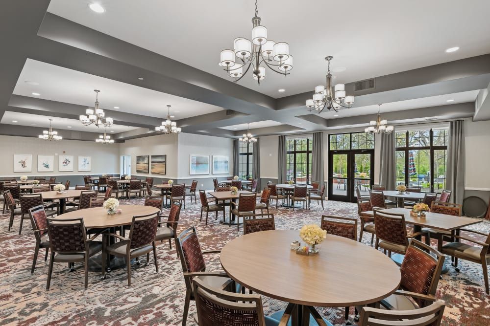 A spacious and elegant dining room with round tables, upholstered chairs, and multiple chandeliers.
