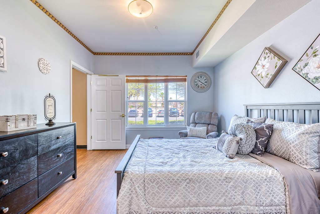 A cozy bedroom with a neatly made bed, a large window allowing natural light, and stylish decor.