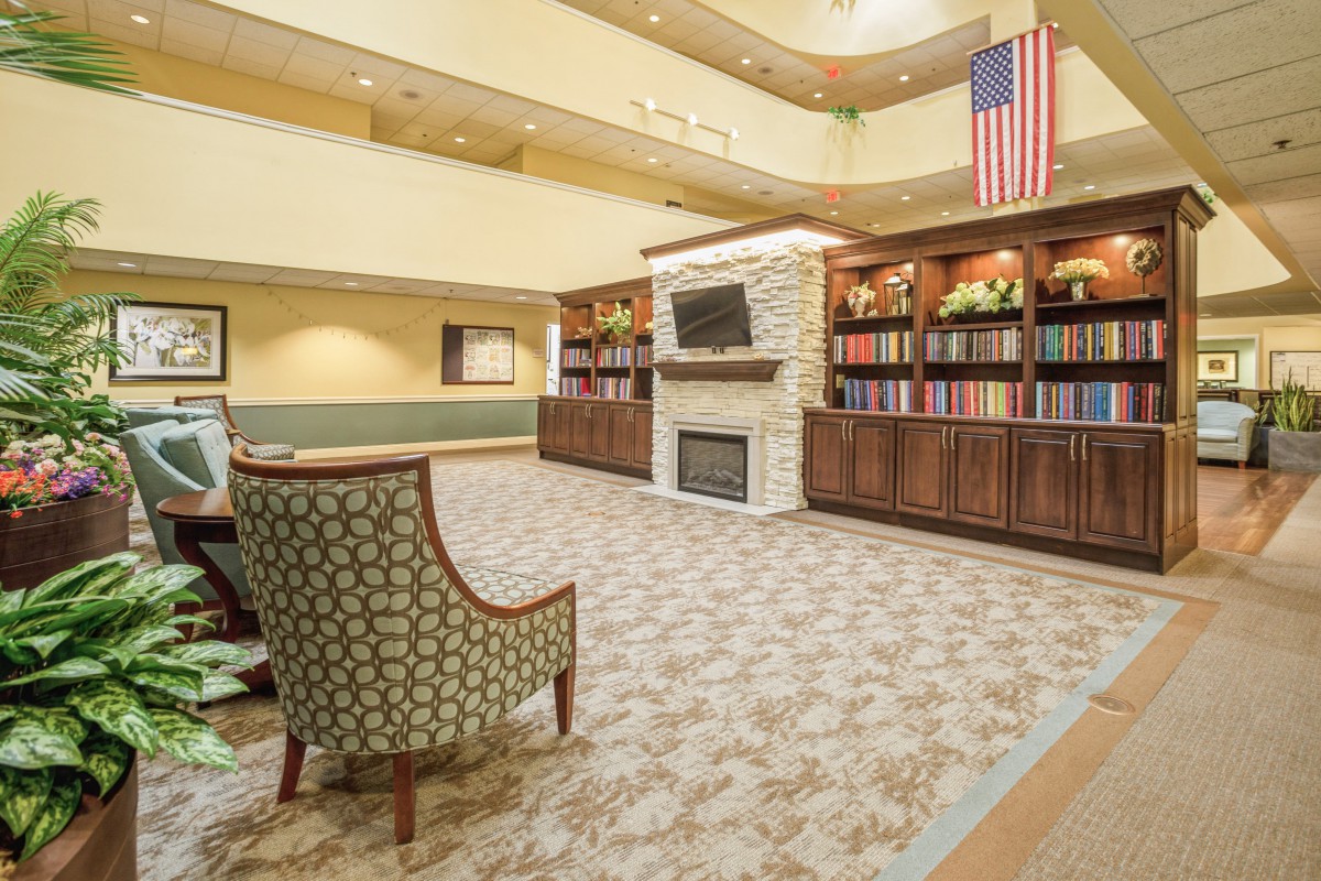 A spacious lobby with a fireplace, bookshelves, and seating area under an atrium with an American flag.