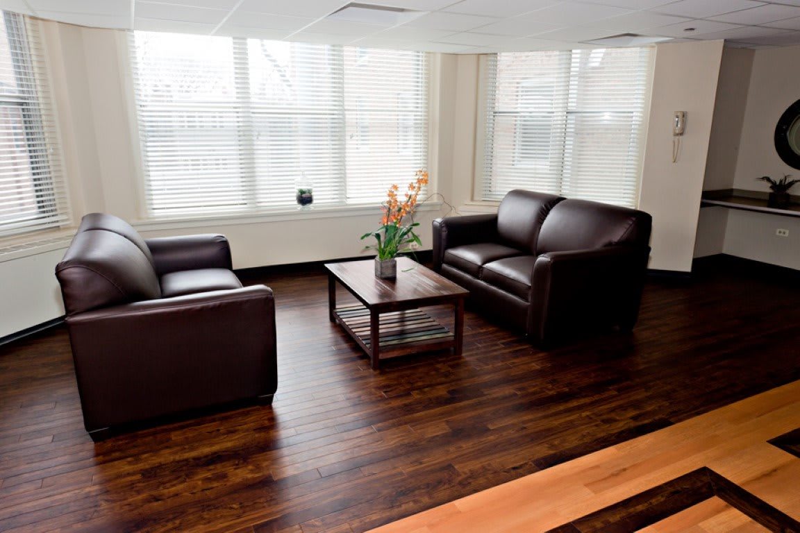 A modern living room with two leather sofas and a wooden coffee table on a hardwood floor, featuring large windows.