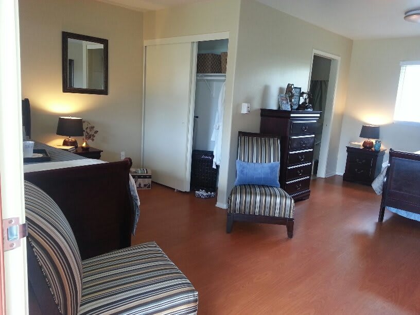 A cozy bedroom with modern furniture, featuring a striped chair, dresser, and hardwood flooring.