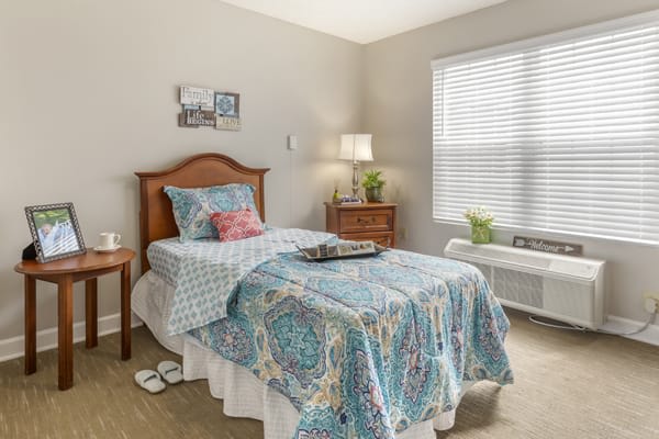 A cozy, well-lit bedroom with a single bed adorned with a colorful quilt and matching pillows.