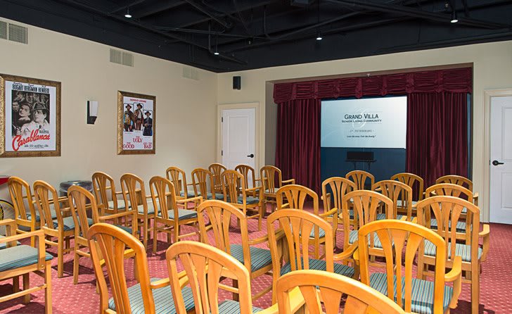 A small conference room with wooden chairs arranged in rows facing a projector screen.