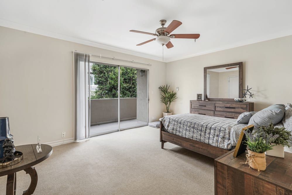 A spacious bedroom with a large bed, ceiling fan, sliding door to the balcony, and neutral decor.