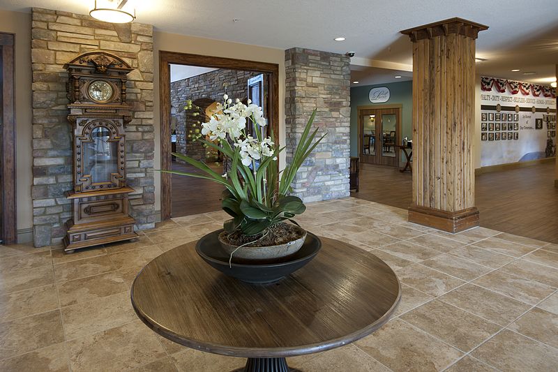 A stylish lobby interior featuring a wooden table with an orchid centerpiece, surrounded by stone walls and warm decor.